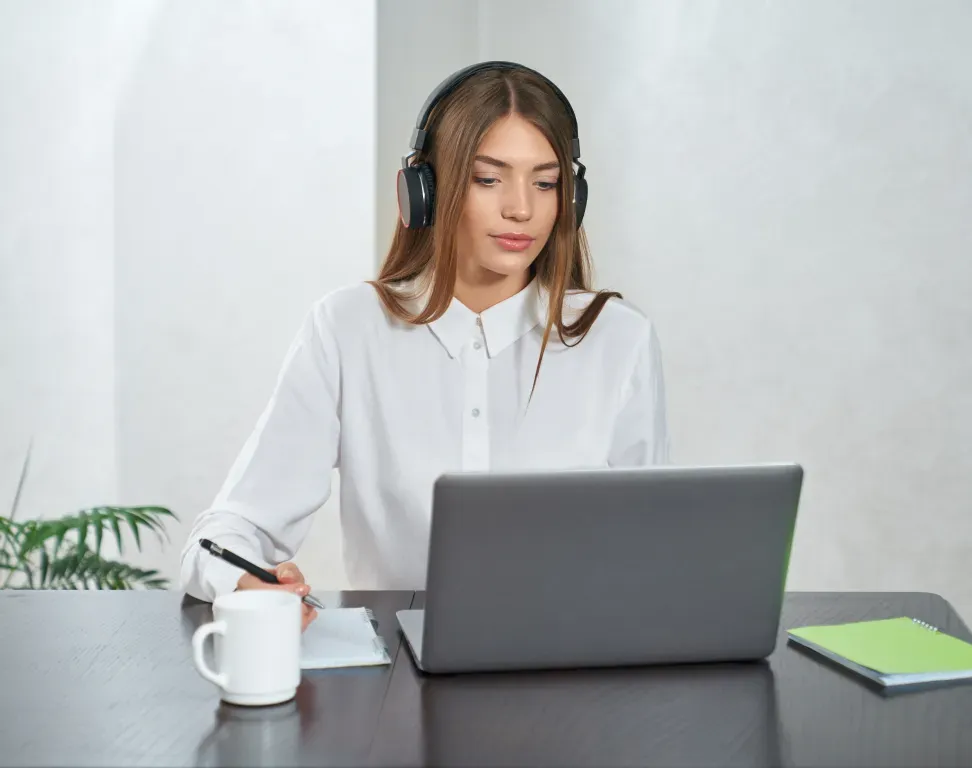 Woman wearing headphones taking notes at a laptop